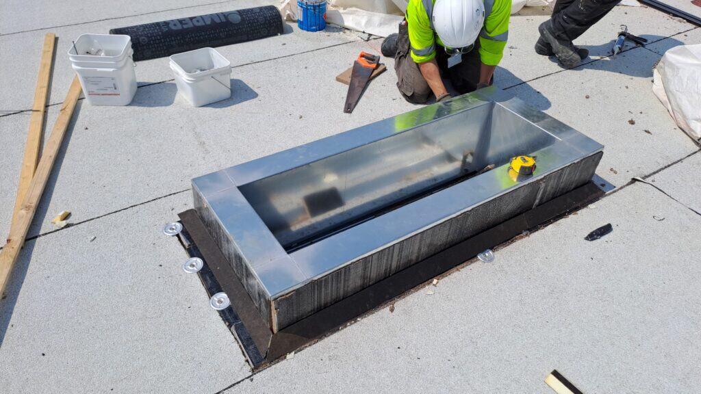 Worker installing roof skylight with tools.