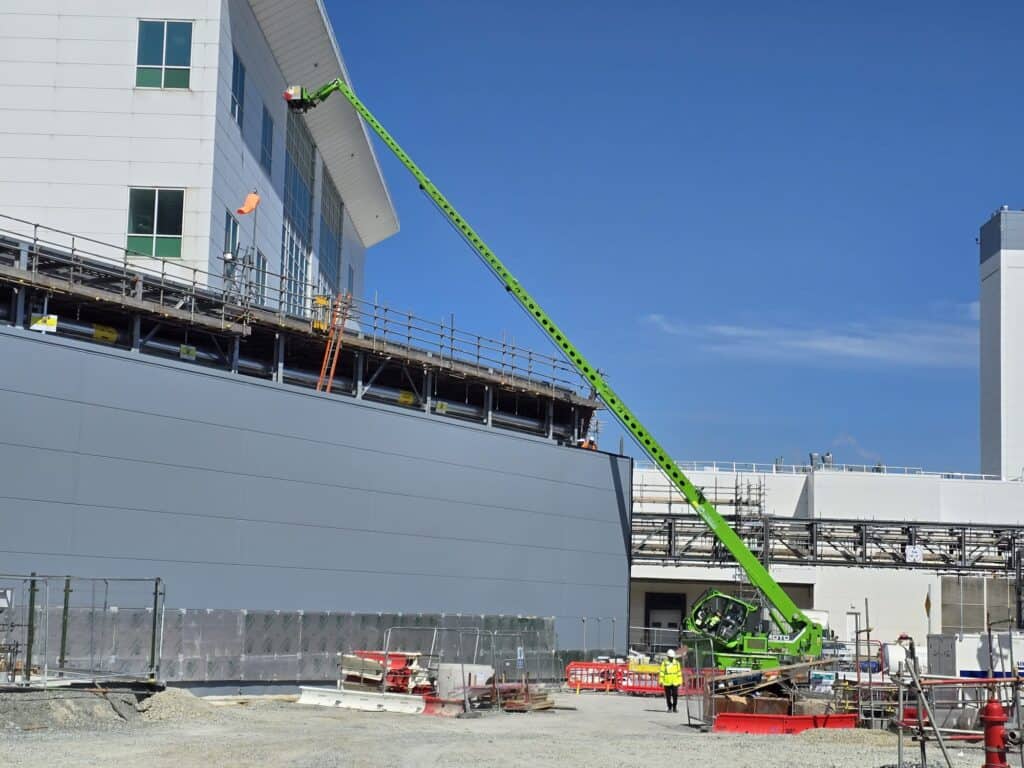 Green telescopic handler at construction site near building.